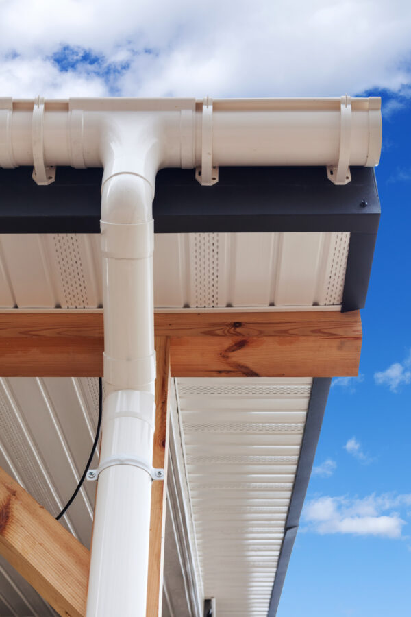 SIP panel house construction. New white rain gutter.  Drainage System with Plastic Siding Soffits and Eaves against blue sky